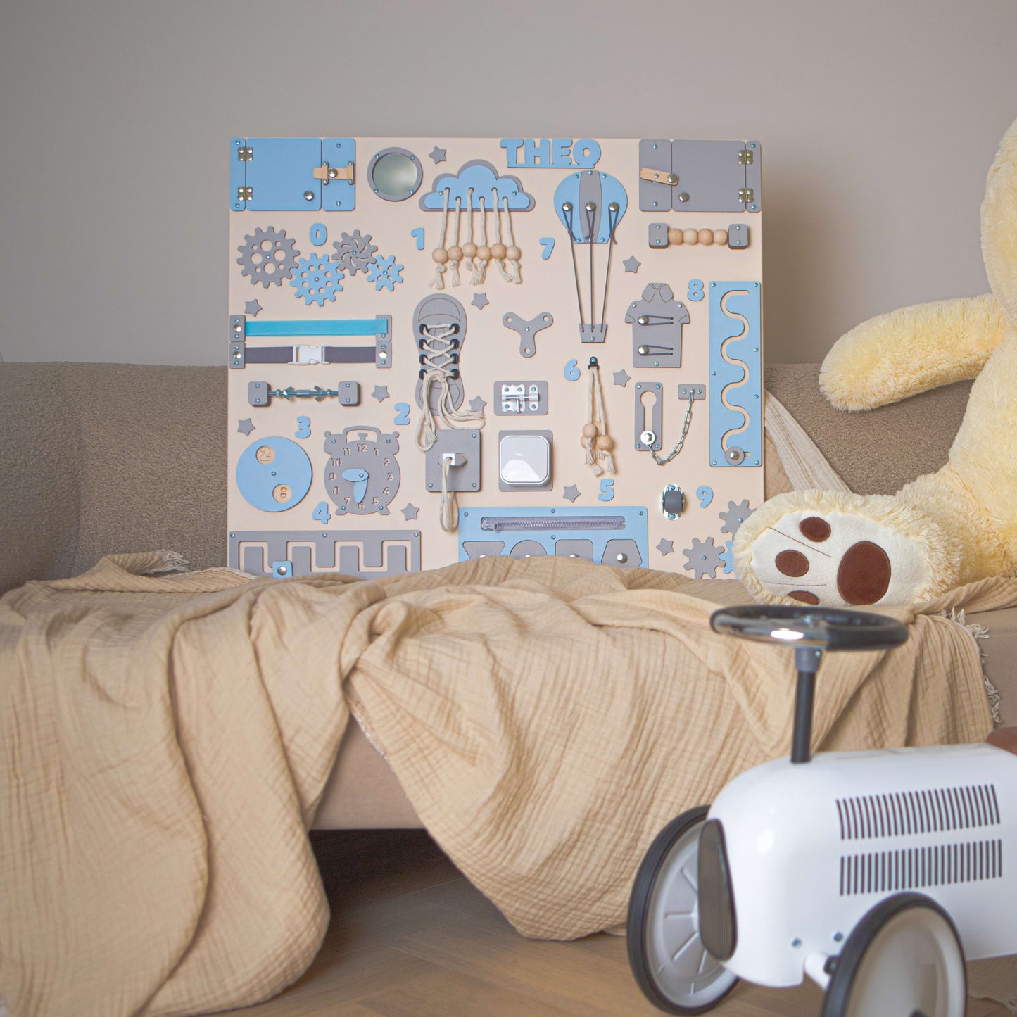 Tableau Montessori bleu pour enfants avec un ours en peluche et une petite voiture sur un canapé.