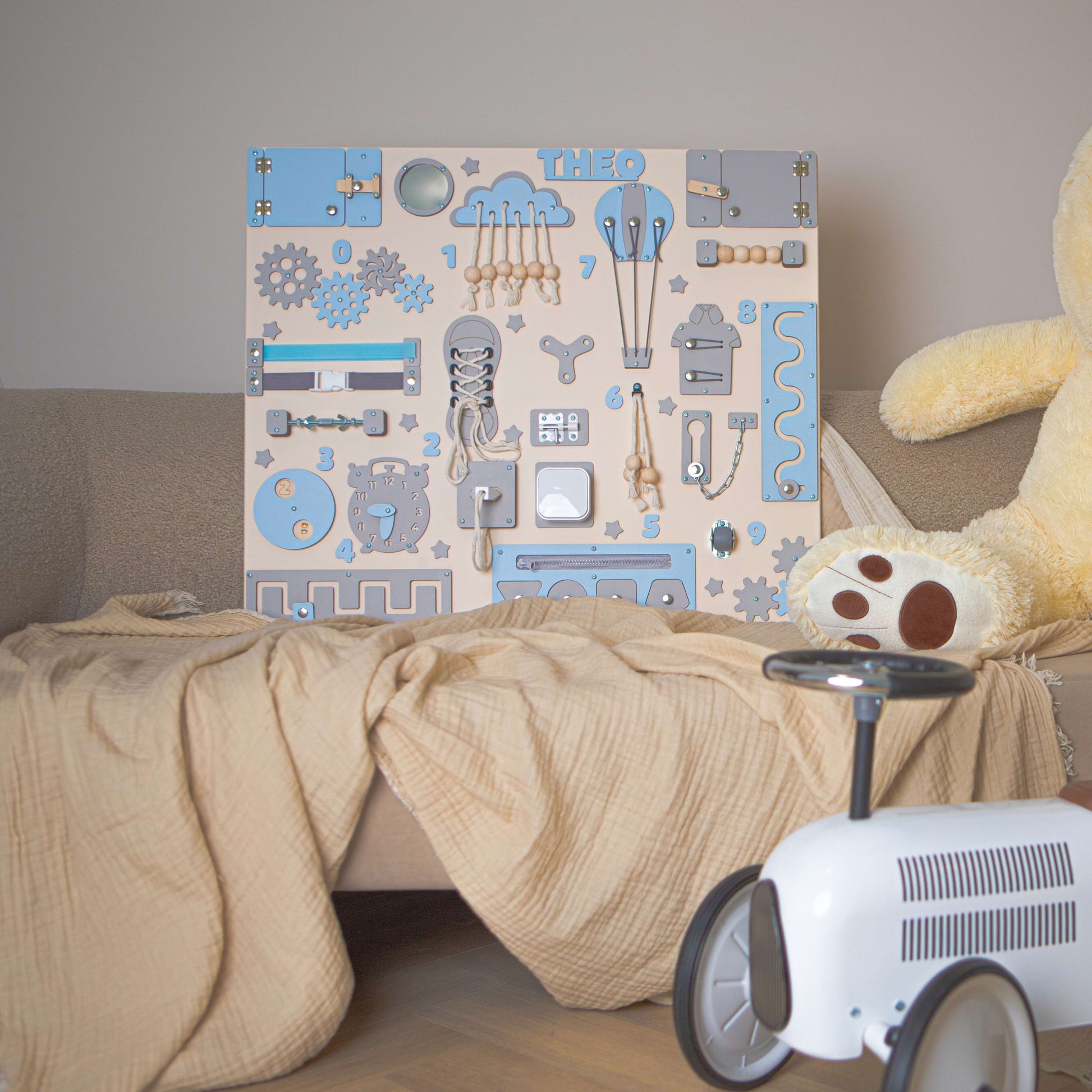 Tableau Montessori bleu pour enfants avec un ours en peluche et une petite voiture sur un canapé.