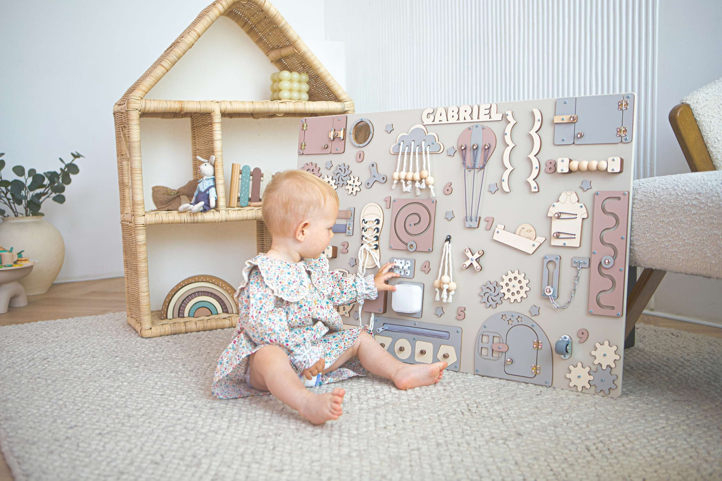 Kind spielt mit einem Beschäftigungsbrett in einem Zimmer mit Puppenhaus und Pflanzen.
