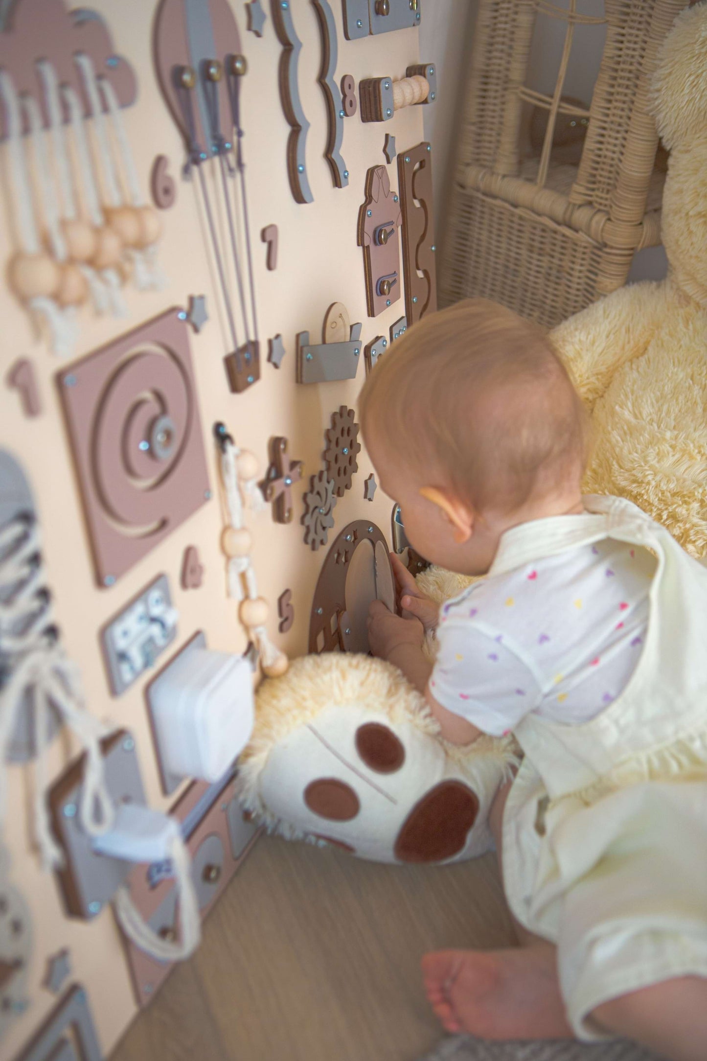 Bébé jouant avec un mur de jouets en bois présentant différentes formes et textures.