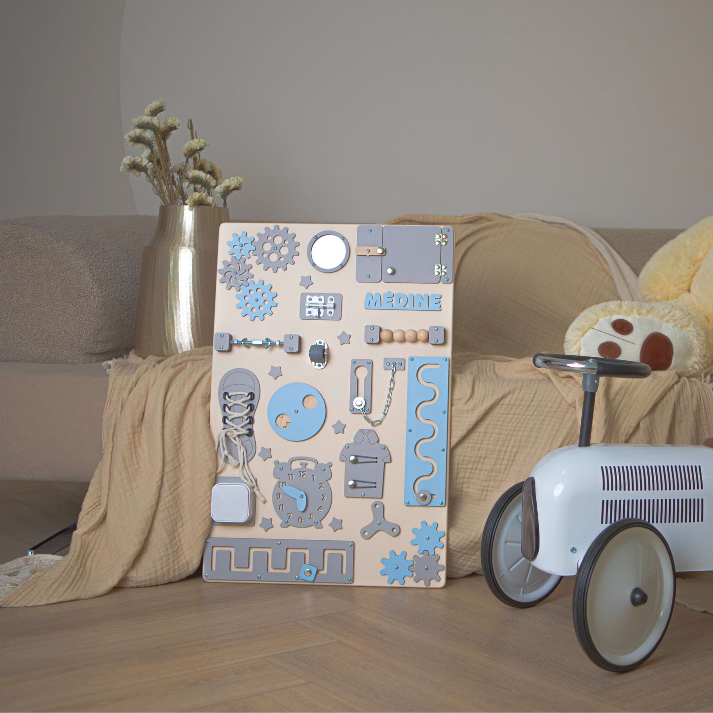 Holz-Aktivitätsbrett mit blauen und grauen Mustern auf einem Holzboden neben einem Kinderspielzeugauto.