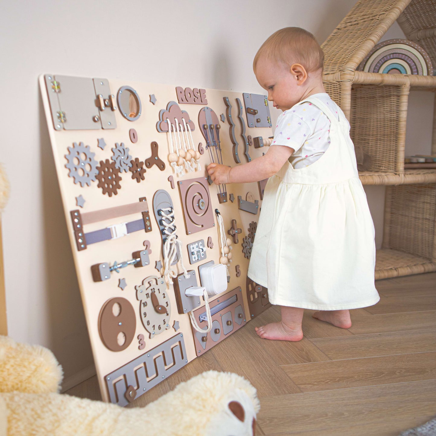 Kind spielt mit einem busy board in einem Zimmer mit einem Korbstuhl.