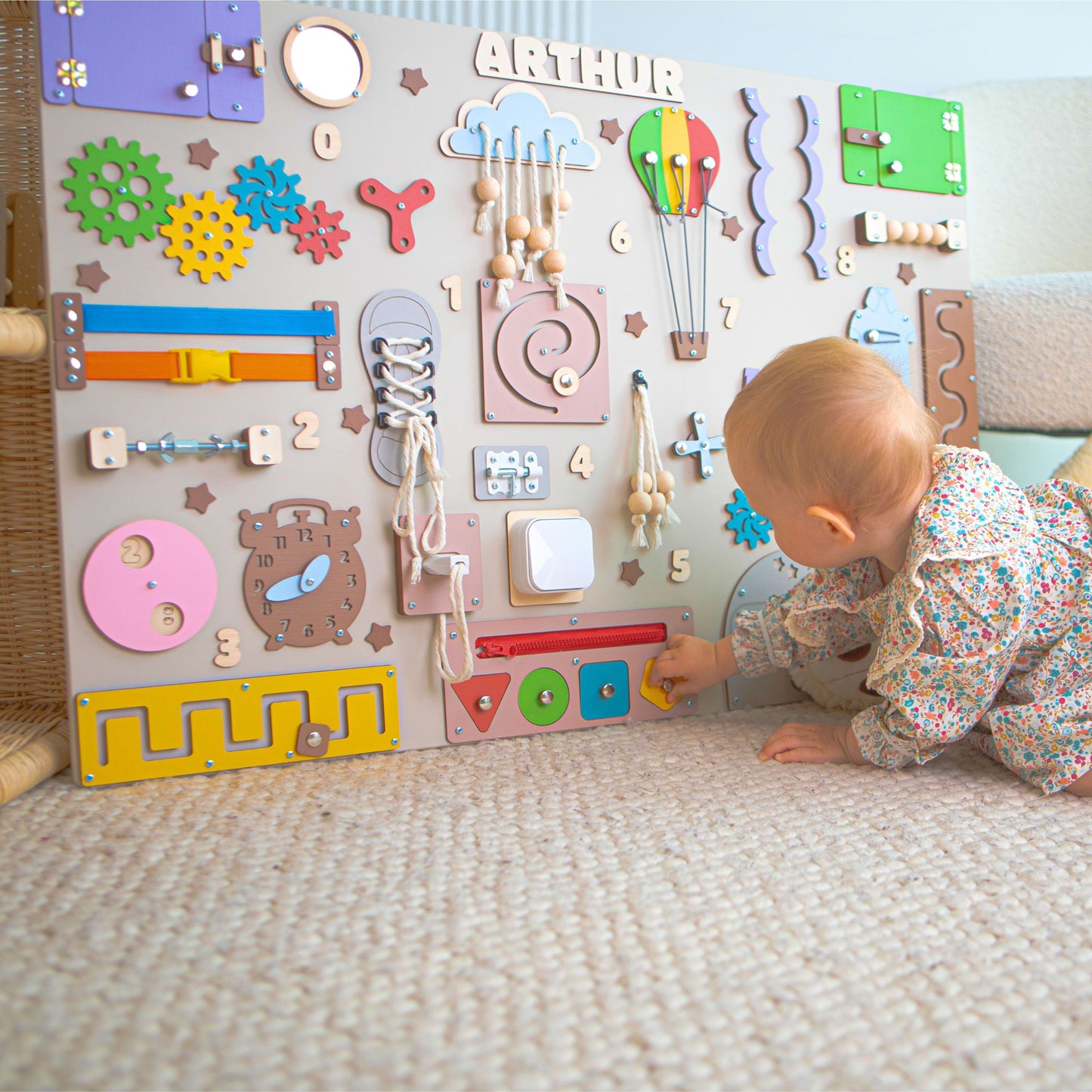 Baby playing with a colorful educational wall panel in a room.