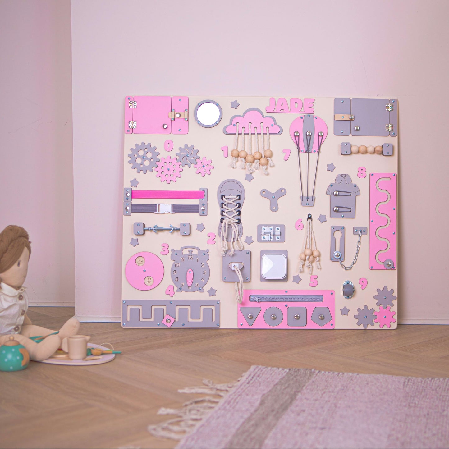 Children's pink busy board with various shapes and designs on a wooden floor.