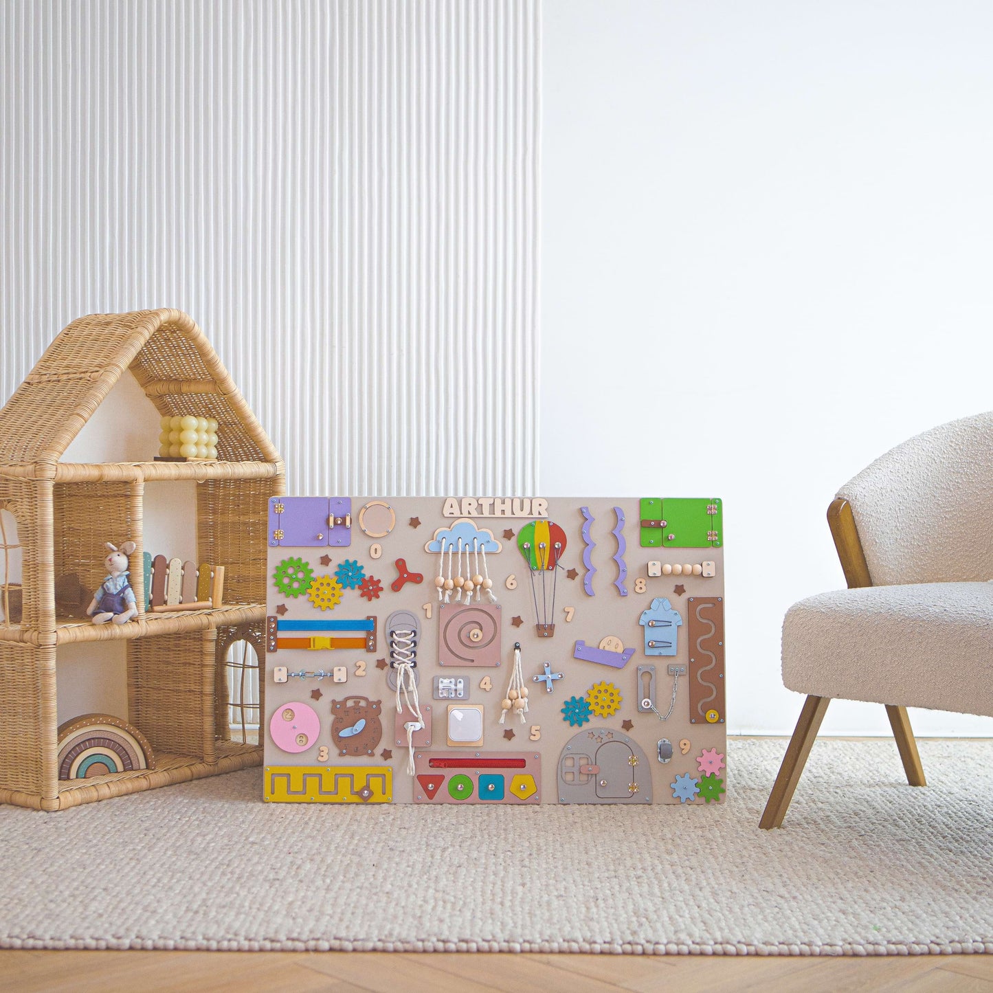 Busy board pour enfants avec différentes formes et motifs dans une pièce avec une maison de poupées et une chaise.
