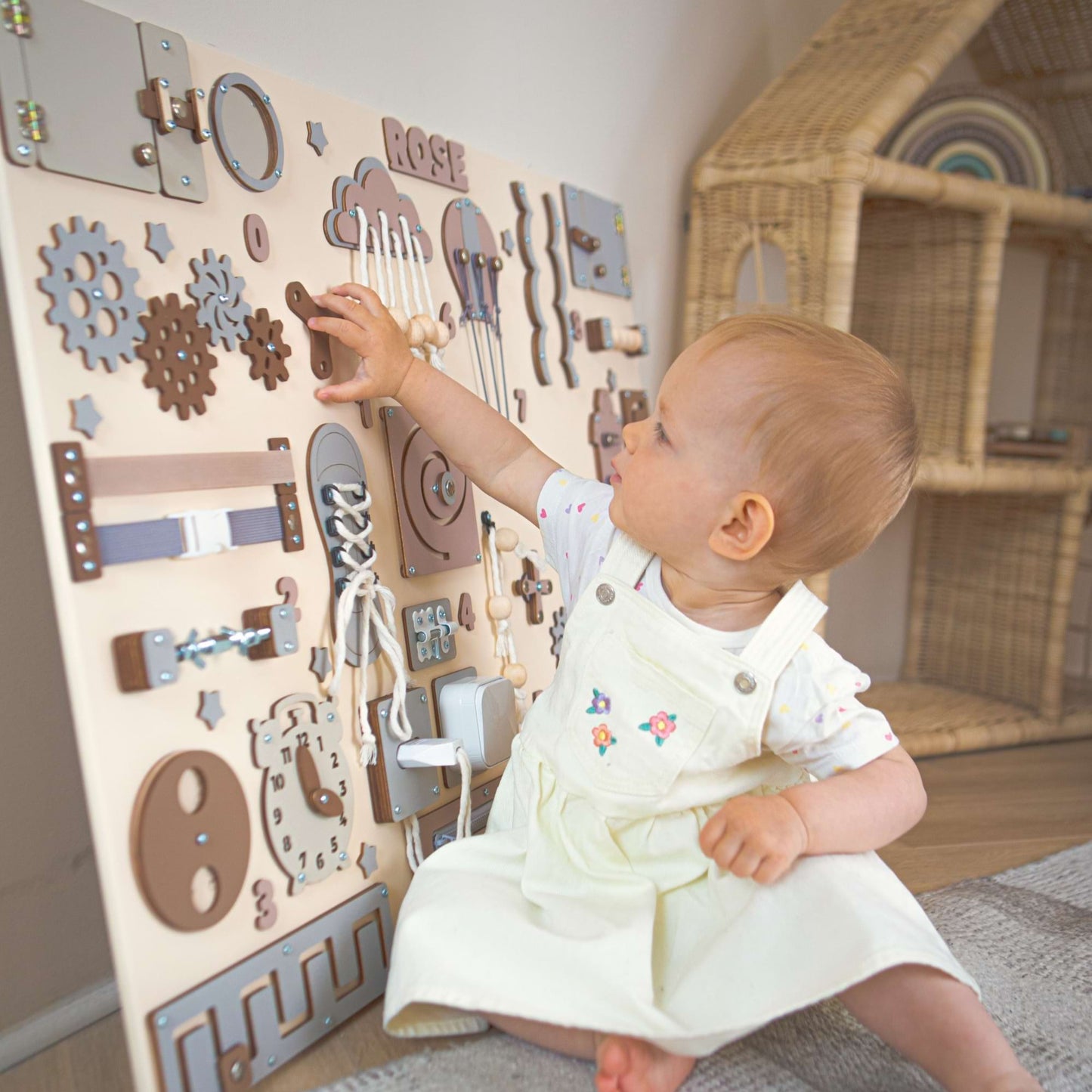 Bébé jouant avec un busy board en bois dans une pièce avec une maison de poupées.