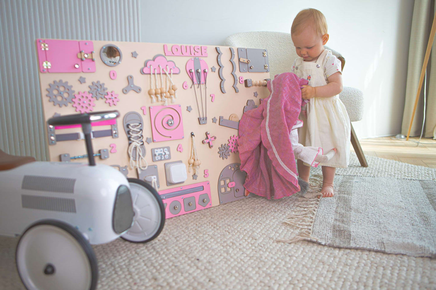 Child playing with a toy wall panel in a room with a rug and chair.
