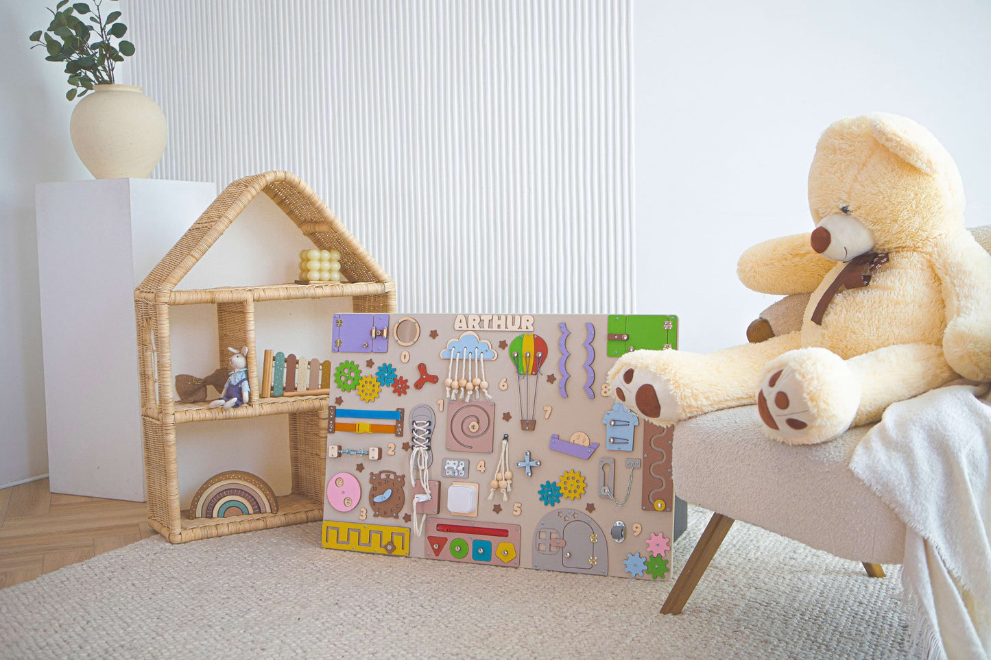 Children's play area with a teddy bear, wooden montessori wall, and educational toy box.