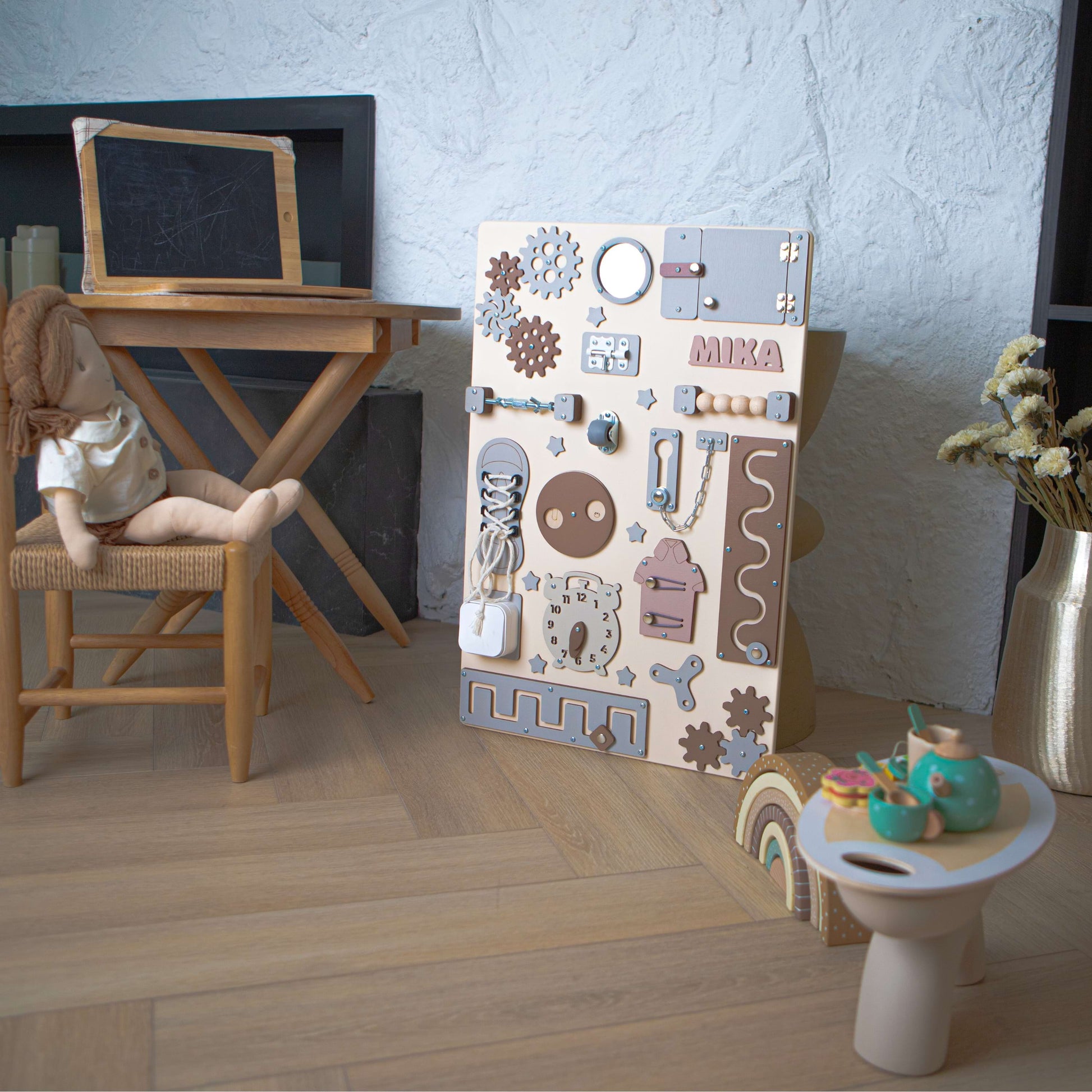 Aire de jeux pour enfants avec un tableau d'activités en bois, une poupée et une petite table.
