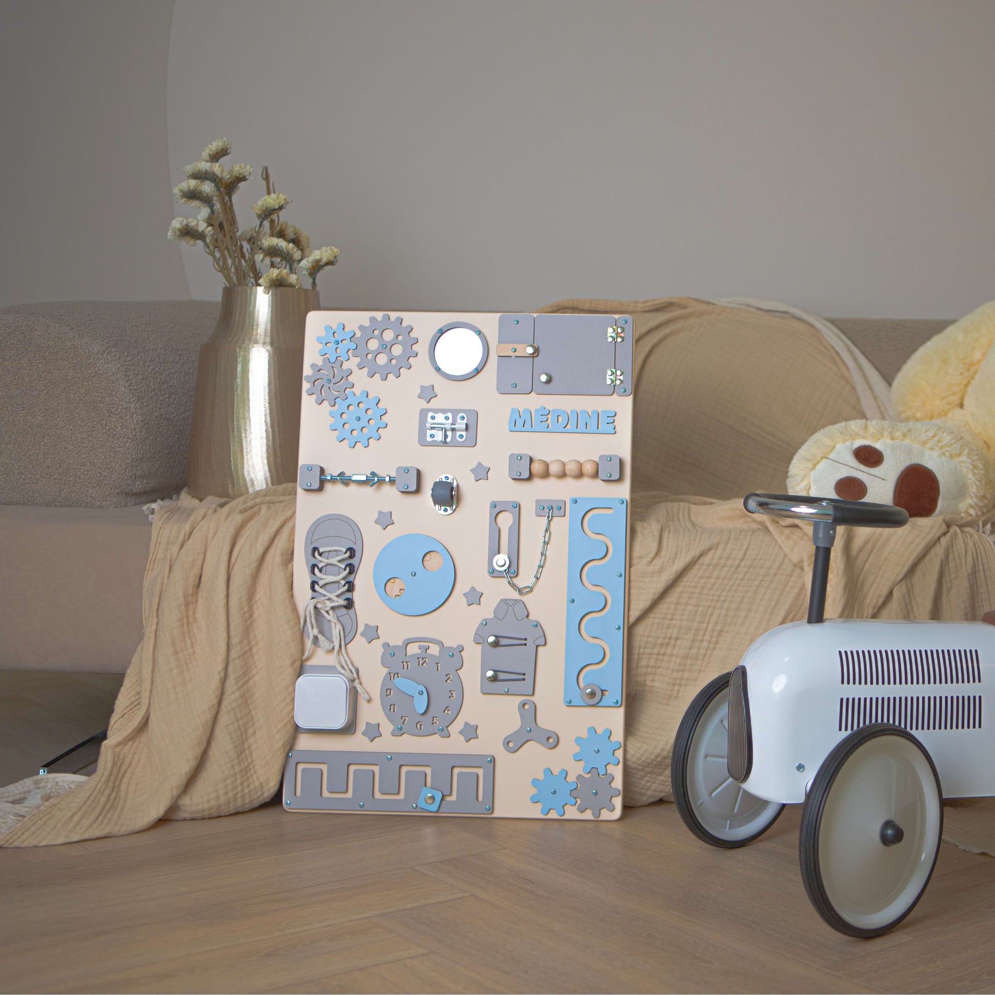 Holz-Aktivitätsbrett mit blauen und grauen Mustern auf einem Holzboden neben einem Kinderspielzeugauto.