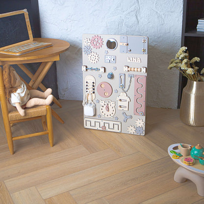 Aktivitätsbrett für Kinder mit verschiedenen pädagogischen Elementen auf einem Holzboden.