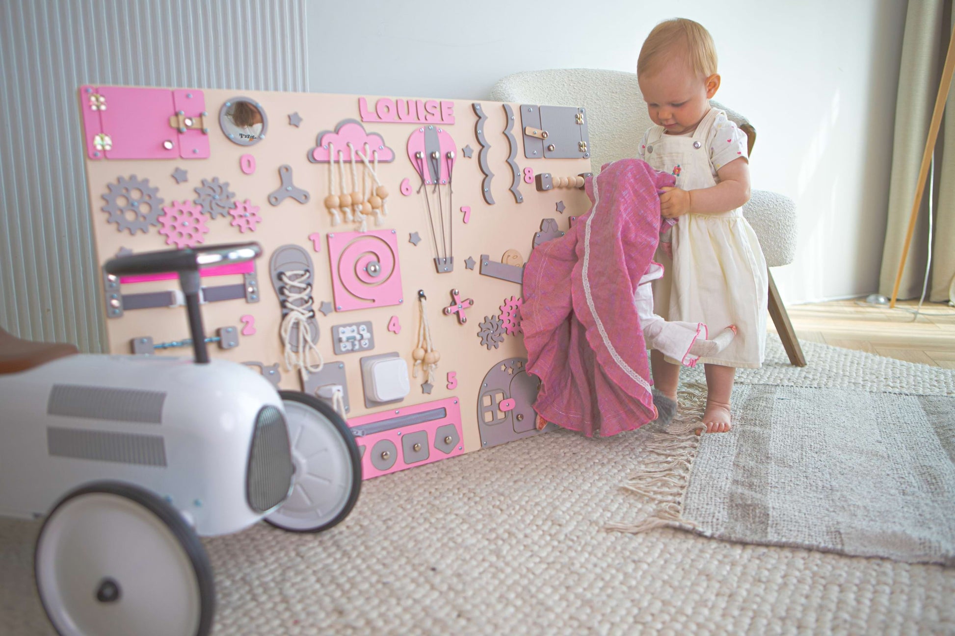 Child playing with a toy wall panel in a room with a rug and chair.