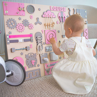 Baby spielt mit einem pädagogischen Spielbrett mit verschiedenen interaktiven Elementen.